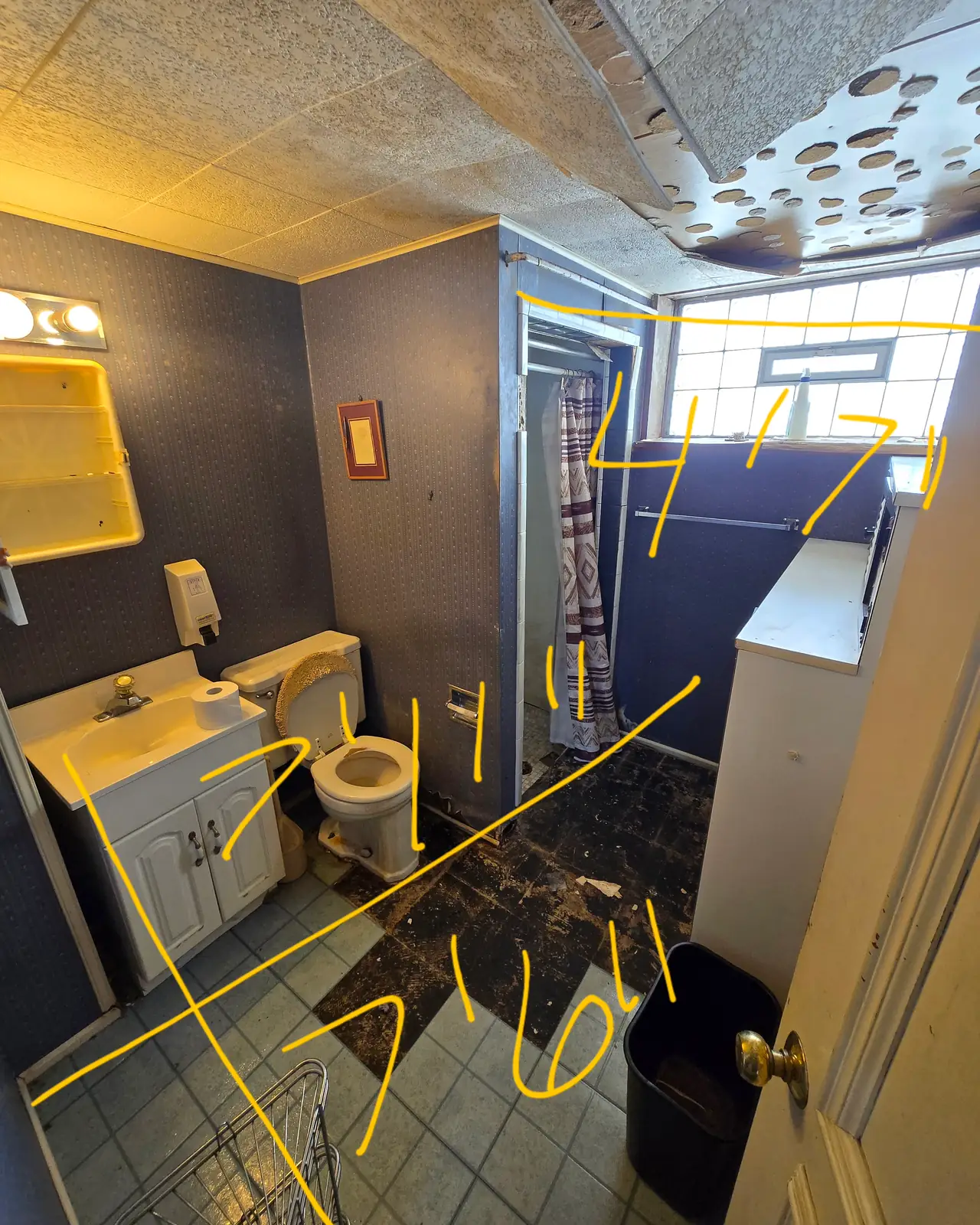 Bathroom with dark walls, a vanity, toilet and corner shower, marked with handwritten measurements, before