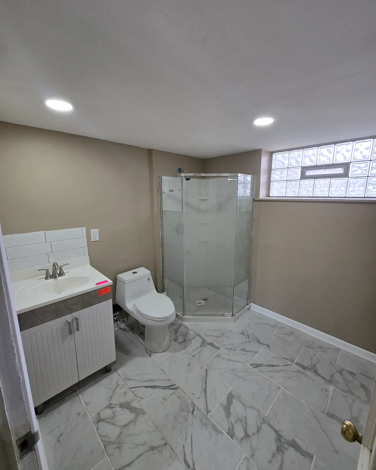 Bathroom with a corner glass shower, white vanity and marble-look floor tile
