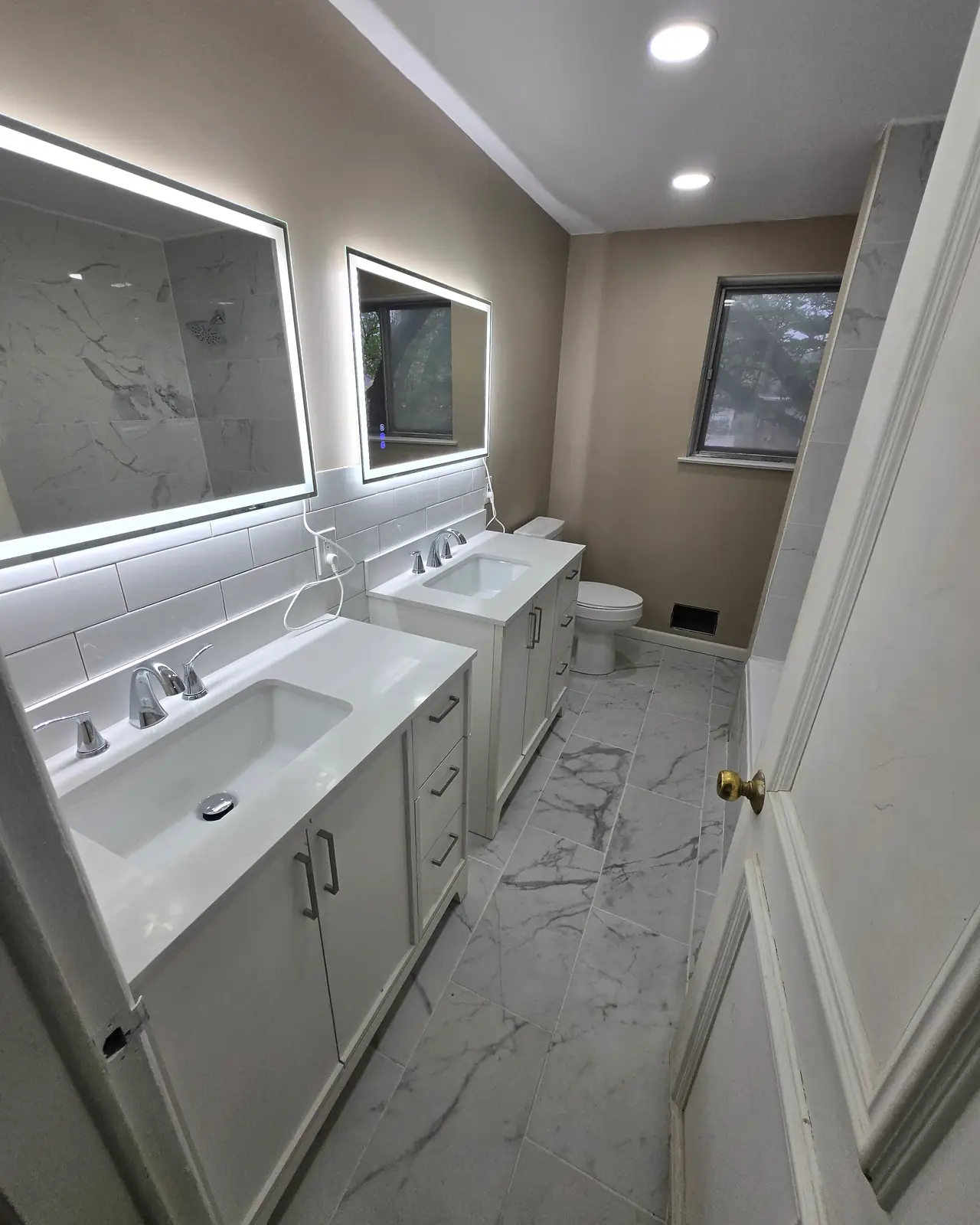 Two white vanities with lighted mirrors and marble-look floor tile