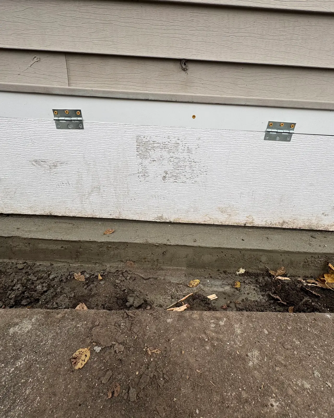 New white framed access panel on a concrete sill below the siding, after