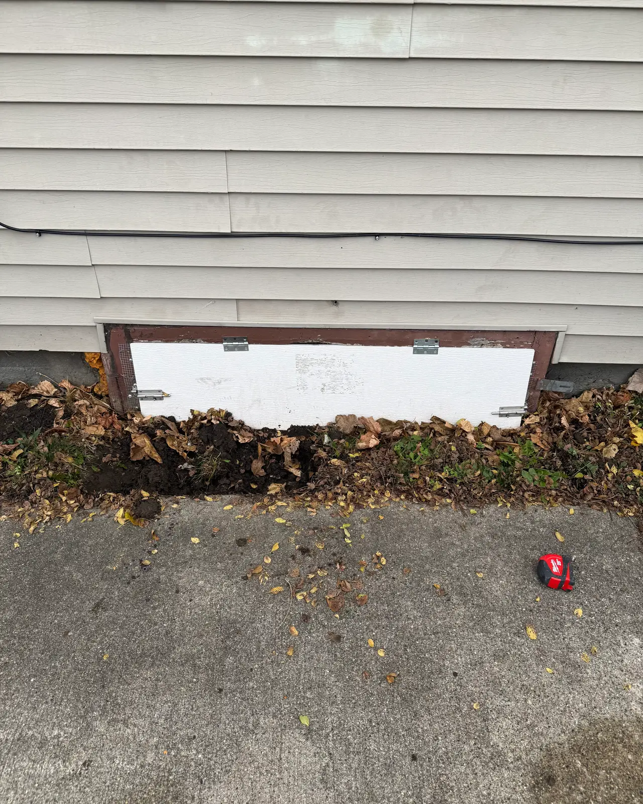 Old access panel in the foundation below vinyl siding, before