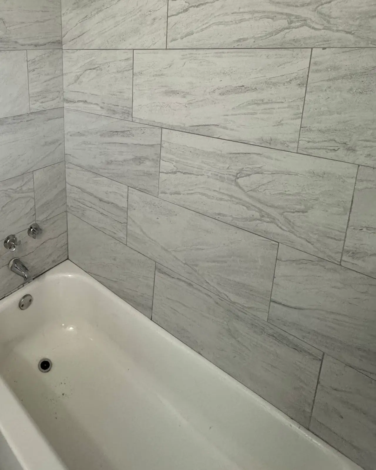 Tub with large gray tile surround and a brass shower head
