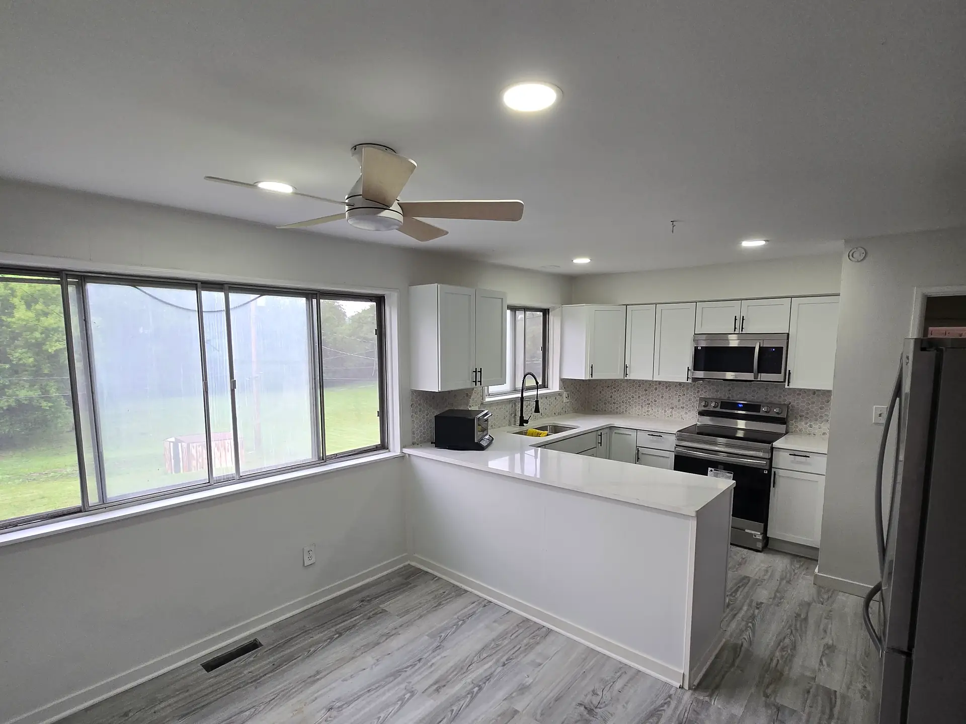 Kitchen with white shaker cabinets, white countertops, stainless appliances and gray plank flooring