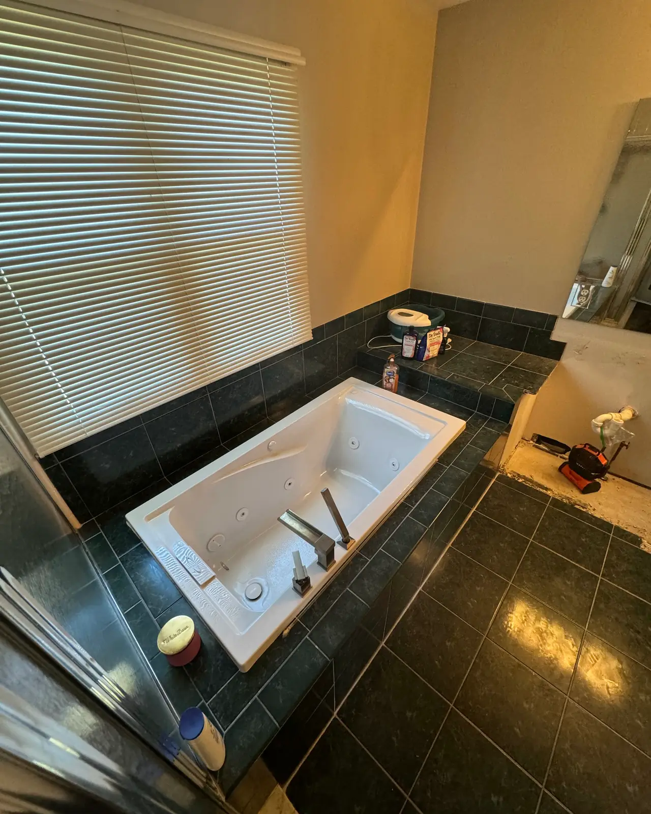 Jetted tub set in dark green tile under a window, before