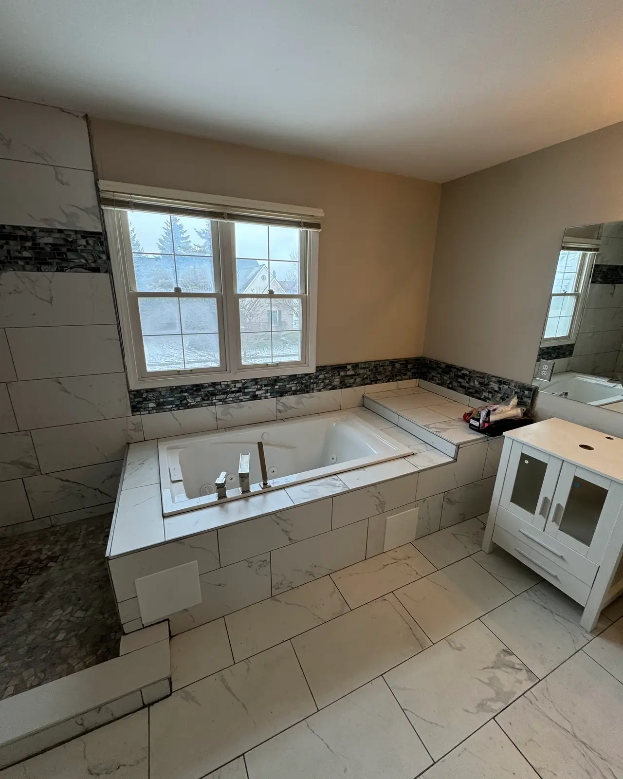 Jetted tub surrounded by white tile with a mosaic accent band, after