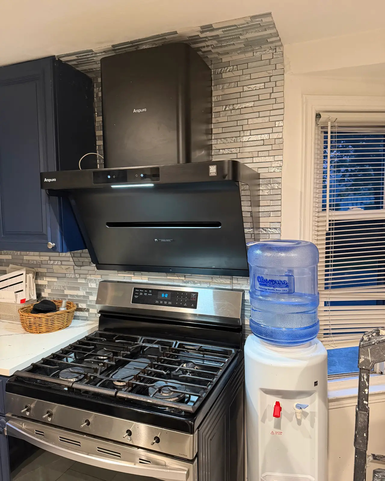 Gas range under a black wall hood with a glass and stone tile backsplash