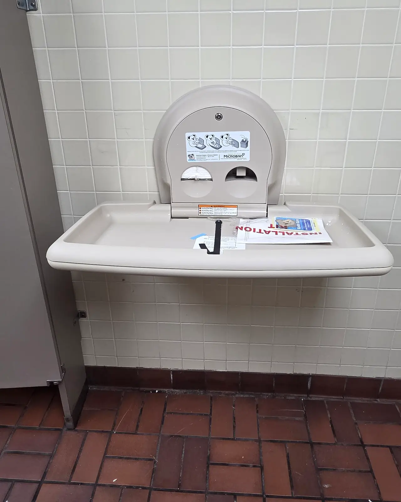 New baby changing station mounted on a tiled restroom wall