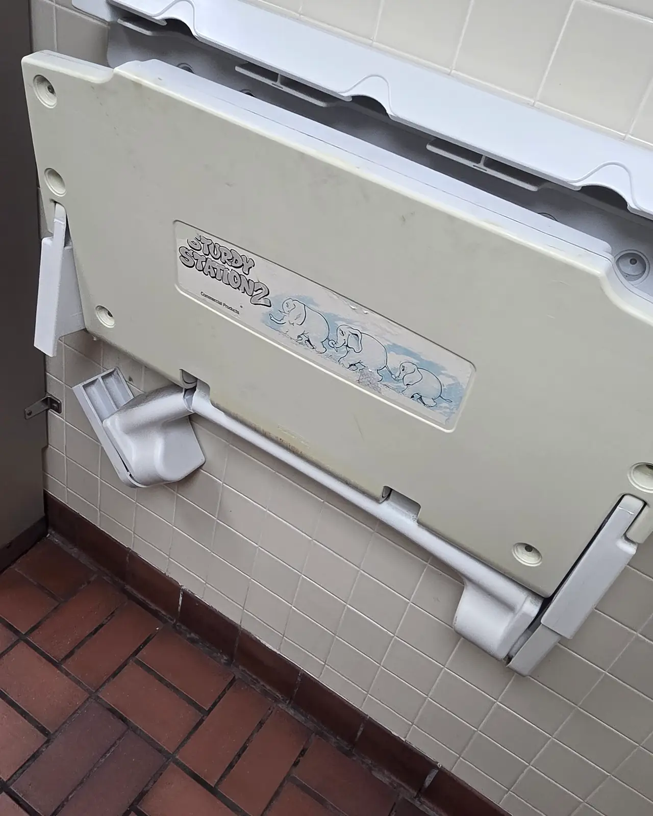 Old baby changing station hanging loose from a tiled restroom wall, before